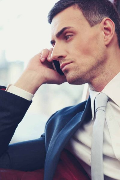 Confident businessman talking on the phone and looking in window at office